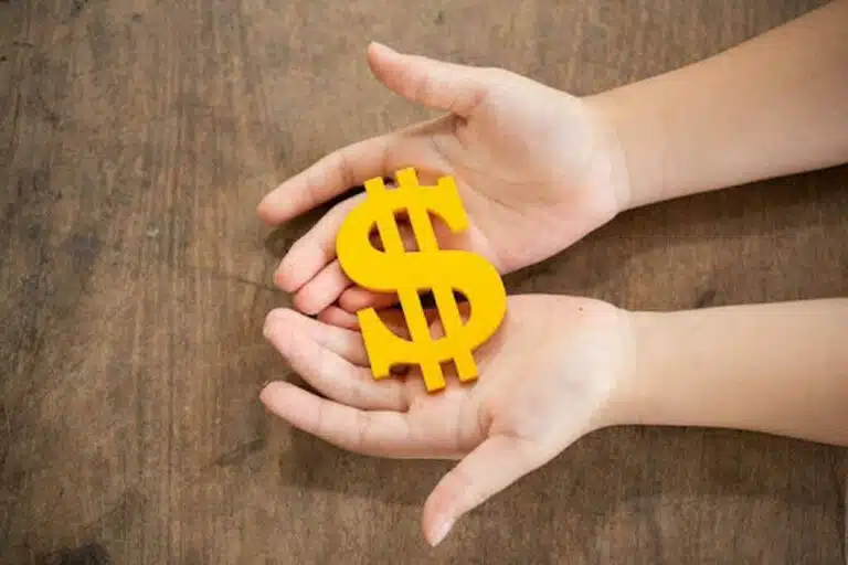 Imagem de duas mãos segurando um símbolo de dinheiro sobre uma mesa, representando o capital social da empresa.