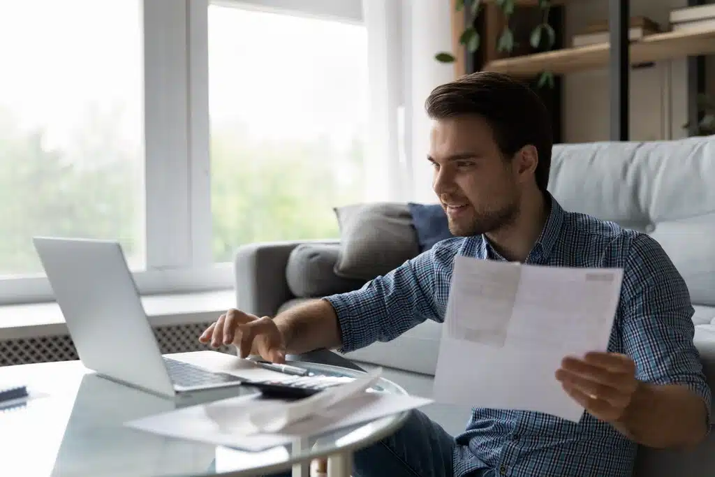 homem segurando um papel e mexendo em um notebook, representando o tema serviços contábeis