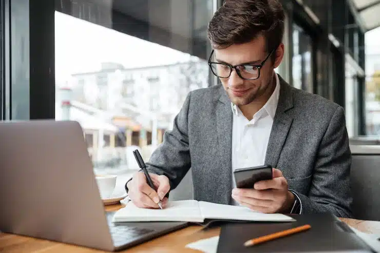 Empresário fazendo cálculo no celular e anotações na agenda